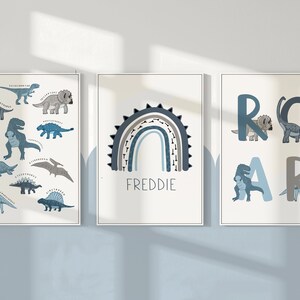 May include: Three framed dinosaur-themed art prints. One features various dinosaur illustrations with their names. Another displays a rainbow with the name "FREDDIE". The third spells "ROAR" with dinosaur illustrations.