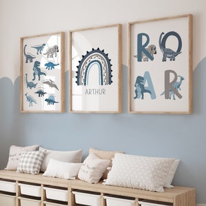 May include: Three framed art prints with a dinosaur theme. One print features various dinosaur illustrations, another displays a blue rainbow with the name "ARTHUR", and the third spells "ROAR" with dinosaur graphics. The prints are in wooden frames.