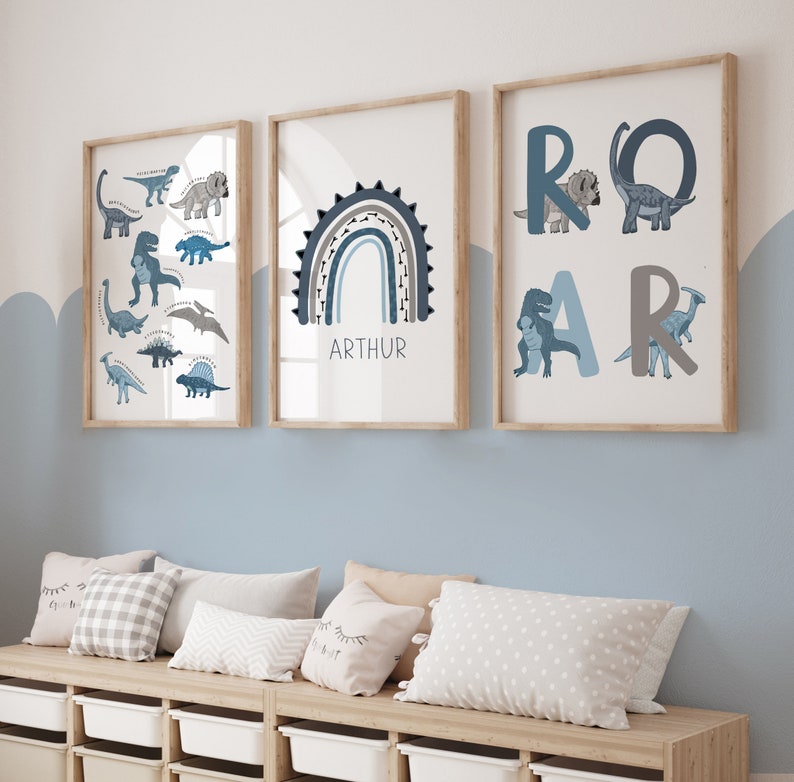May include: Three framed art prints with a dinosaur theme. One print features various dinosaur illustrations, another displays a blue rainbow with the name "ARTHUR", and the third spells "ROAR" with dinosaur graphics. The prints are in wooden frames.