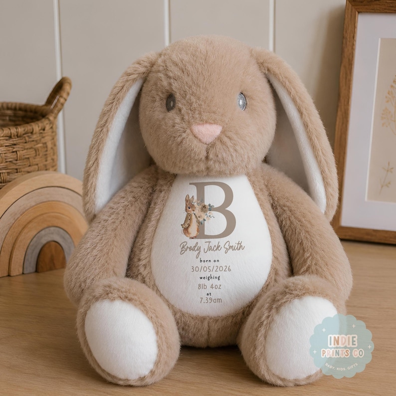 May include: A plush tan rabbit toy with long ears and white paw pads. The white belly features a printed design with a large letter B, a small rabbit illustration, and the text: Brody Jack Smith, born on 30/05/2026, weighing 8lb 4oz at 7.39am.