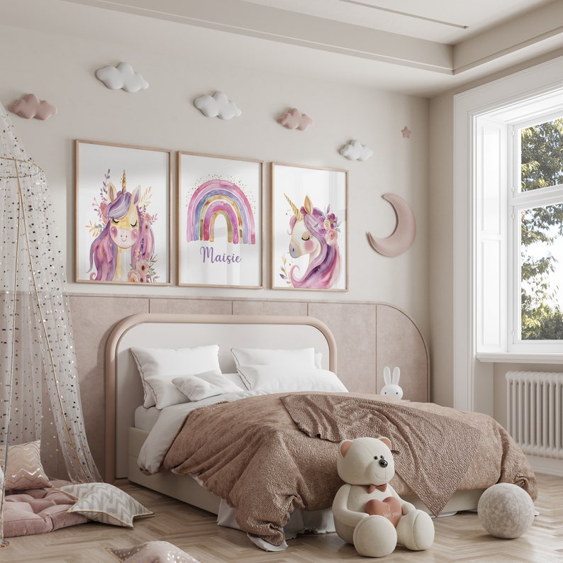 Puede incluir: Una habitaci&oacute;n infantil con una cama con edred&oacute;n marr&oacute;n y almohadas blancas. Encima de la cama, tres impresiones art&iacute;sticas enmarcadas de unicornios con detalles florales y una impresi&oacute;n de arco&iacute;ris con el nombre "Maisie". Nubes decorativas adornan la pared.
