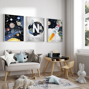 May include: Three framed space-themed art prints. One depicts the solar system, another features the letter "N" and the name "Noah", and the third shows a rocket ship. The room also includes a small desk, chair, and a plush rug.