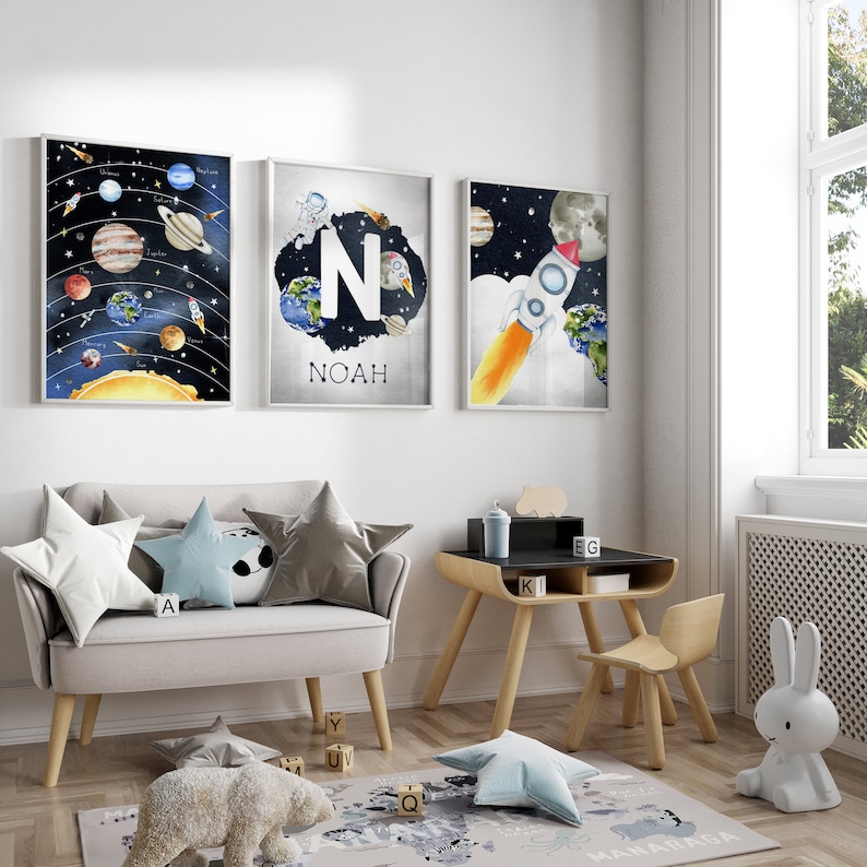 May include: Three framed space-themed art prints. One depicts the solar system, another features the letter "N" and the name "Noah", and the third shows a rocket ship. The room also includes a small desk, chair, and a plush rug.