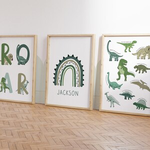 May include: Three framed art prints with a dinosaur theme. One print spells "ROAR" with dinosaur illustrations. Another features a green and brown rainbow with the name "JACKSON". The third print displays various dinosaur species.