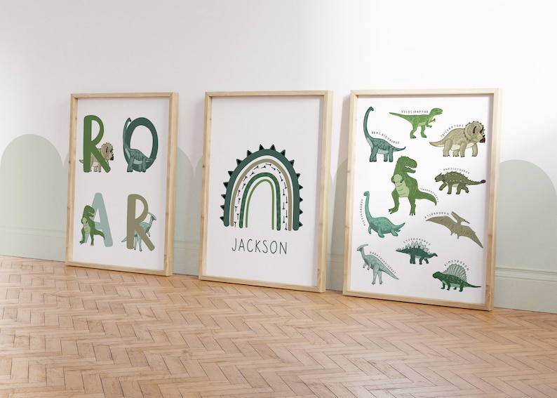 May include: Three framed art prints with a dinosaur theme. One print spells "ROAR" with dinosaur illustrations. Another features a green and brown rainbow with the name "JACKSON". The third print displays various dinosaur species.