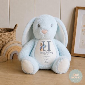 May include: A light blue plush rabbit toy with long ears and a white belly patch. The patch features a Peter Rabbit illustration, the letter H, and the text: Harris Joe Thomas, born on 05/29/2026, weighing 6lb 11oz, at 6.22pm.