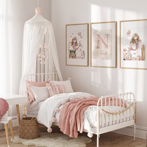 May include: A child's bedroom with a white metal bed, adorned with pink and white bedding and a matching throw blanket. Three framed mermaid art prints hang above the bed. A white canopy with a crown and hanging decorations adds a whimsical touch.