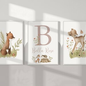 May include: Three framed watercolor prints featuring woodland animals. One print shows a fox, another a deer, and the third a large letter "B" with the name "Bella Rose". The prints have a soft, neutral color palette with green and brown accents.