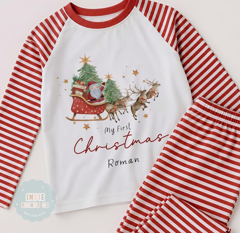 May include: A white long-sleeve pajama set with red and white striped sleeves and pants. The shirt features a graphic of Santa in a sleigh pulled by reindeer, green Christmas trees, and gold stars. Text reads My First Christmas Roman.