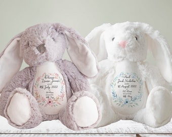 May include: Two plush bunny rabbits, one gray and one white, with embroidered details. Each bunny has a floral wreath design with personalized text. The gray bunny has a pink nose and the white bunny has a pink nose.