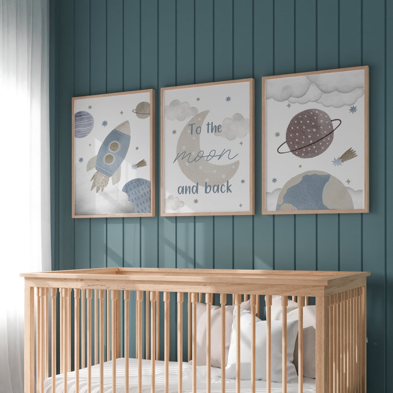 May include: Three framed art prints with a space theme hang above a wooden crib. The prints feature a rocket, a crescent moon with the text "To the moon and back," and a planet. The color palette includes blue, brown, and beige.