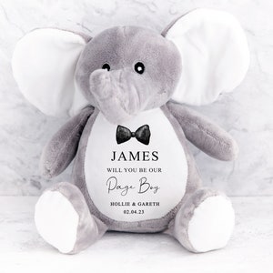 Pode incluir: Um brinquedo de pel&uacute;cia de elefante cinzento com grandes orelhas brancas. O elefante tem uma gravata borboleta preta e o texto "JAMES WILL YOU BE OUR Page Boy HOLLIE & GARETH 02.04.23" impresso no peito. Um presente fofo para um casamento.