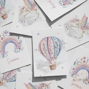 Op de afbeelding: Een verzameling aquarelprints met grillige ontwerpen. De prints tonen een heteluchtballon met een eenhoorn, een regenboog en een Pegasus. Zachte pastelkleuren en bloemaccenten cre&euml;ren een dromerige esthetiek. De naam "Sienna" staat op een print.