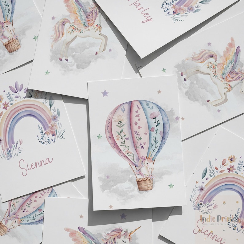 Op de afbeelding: Een verzameling aquarelprints met grillige ontwerpen. De prints tonen een heteluchtballon met een eenhoorn, een regenboog en een Pegasus. Zachte pastelkleuren en bloemaccenten cre&euml;ren een dromerige esthetiek. De naam "Sienna" staat op een print.