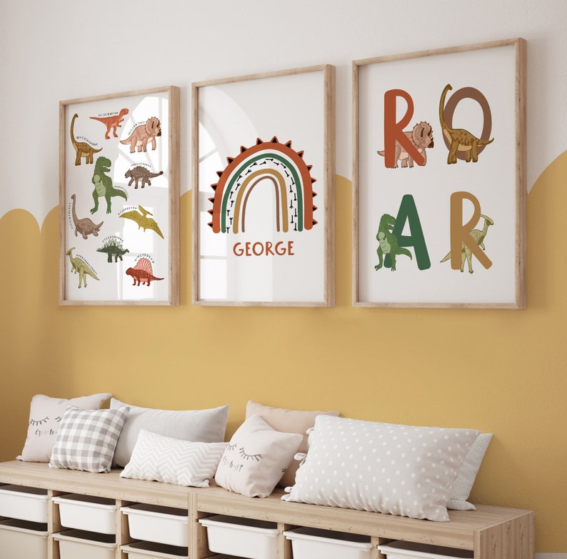 May include: Three framed art prints with a dinosaur theme. One print features various dinosaur illustrations, another has a rainbow with the name "GEORGE", and the third spells "ROAR" with dinosaur figures. The frames are light wood.