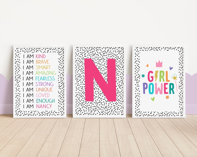 May include: Three framed prints with white backgrounds and black polka dots. One print has the text "I AM KIND, BRAVE, SMART, AMAZING, FEARLESS, STRONG, UNIQUE, LOVED, ENOUGH, NANCY" in rainbow colors. Another features a large pink letter "N". The third says "GIRL POWER".