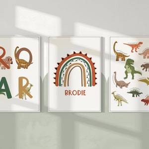 May include: Three framed art prints with a dinosaur theme. One print spells "ROAR" with dinosaur illustrations. Another features a rainbow with the name "BRODIE". The third print displays various dinosaur species.