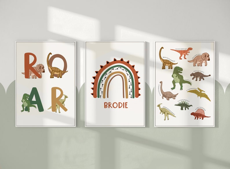 May include: Three framed art prints with a dinosaur theme. One print spells "ROAR" with dinosaur illustrations. Another features a rainbow with the name "BRODIE". The third print displays various dinosaur species.