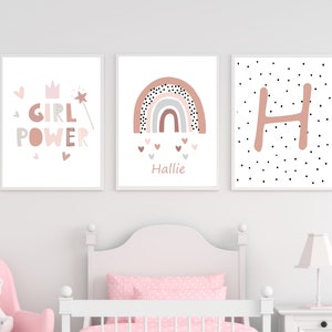 May include: Three framed art prints with a nursery theme. The prints feature the words "GIRL POWER", a rainbow design, and the letter "H". The color palette includes pink, gray, and white, creating a soft and inviting aesthetic.