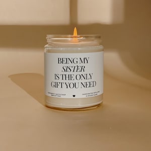 Könnte beinhalten: Eine brennende Sojawachskerze in einem durchsichtigen Glas. Auf dem Etikett steht "BEING MY SISTER IS THE ONLY GIFT YOU NEED". Die Kerze stammt von The Perfect Match Shop, handgefertigt in Rhode Island.