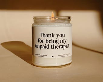 May include: A lit soy wax candle in a clear glass jar. The label reads "Thank you for being my unpaid therapist." The candle is from The Perfect Match Shop and handcrafted in Rhode Island.
