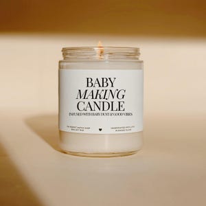 May include: A lit glass candle with a white label that reads "BABY MAKING CANDLE" in black text. The candle is infused with baby dust and good vibes. The candle is handcrafted with love in Rhode Island.