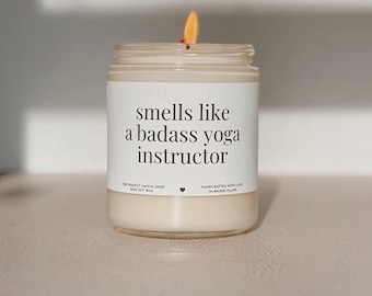 May include: A burning candle in a clear glass jar. The label says "smells like a badass yoga instructor." The candle is made from soy wax and handcrafted in Rhode Island.