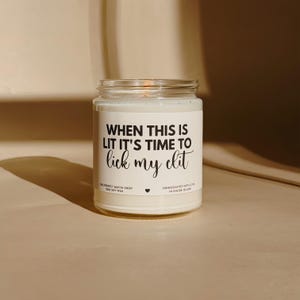 May include: A clear glass jar candle with a white label. The label reads "WHEN THIS IS LIT IT'S TIME TO lick my clit". The candle is made with soy wax and handcrafted in Rhode Island.