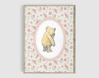 May include: A framed print featuring a watercolor illustration of a yellow bear in an oval frame with a pink lace border. The background is a floral pattern with pink roses on a cream-colored background. The frame is a light brown color.
