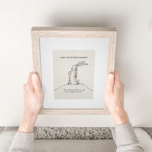 May include: A framed print of "The Velveteen Rabbit" illustration. The artwork features a sketch of a rabbit with the quote "Everything that is real was imagined first." The frame is a light wood color.