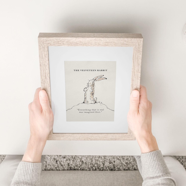 May include: A framed print of "The Velveteen Rabbit" illustration. The artwork features a sketch of a rabbit with the quote "Everything that is real was imagined first." The frame is a light wood color.