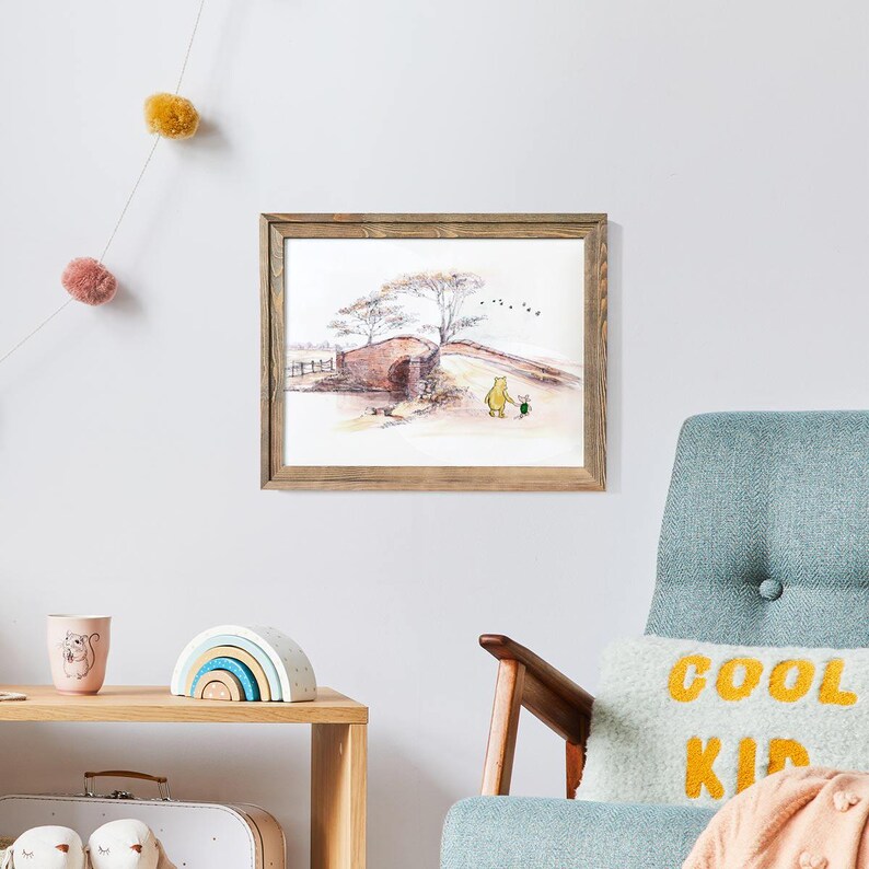 K&ouml;nnte beinhalten: Ein gerahmter Aquarelldruck zeigt eine Br&uuml;ckenszene mit zwei Zeichentrickfiguren. Das Kunstwerk befindet sich in einem rustikalen Holzrahmen. Der Druck weist sanfte Farben und einen skurrilen Stil auf, der f&uuml;r ein Kinderzimmer oder einen Kindergarten geeignet ist.