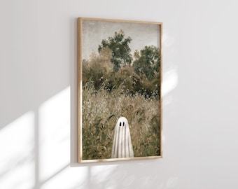 May include: A framed print featuring a whimsical ghost in a field of tall grass and foliage. The artwork has a vintage aesthetic with muted greens, browns, and a white ghost. The wooden frame adds a rustic touch to the Halloween-themed art.