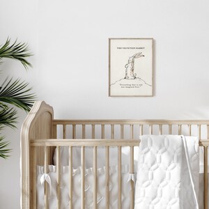 May include: A framed print of "The Velveteen Rabbit" illustration. The artwork features a sketch of a rabbit with the quote "Everything that is real was imagined first." The print is displayed above a wooden crib.