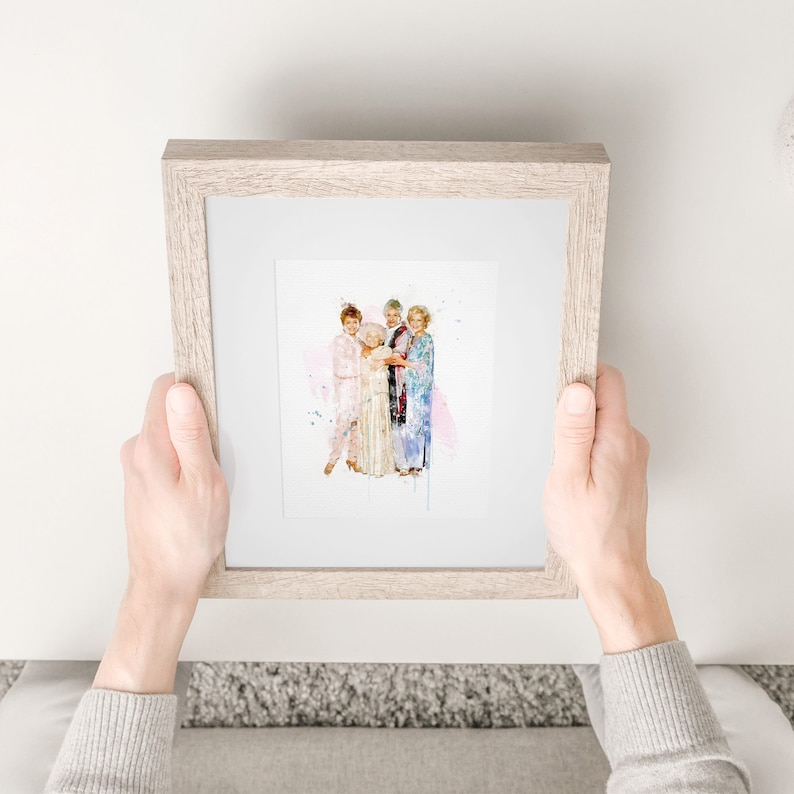 Op de afbeelding: Een ingelijst aquarelprint van vier vrouwen die samen in een groep staan. De vrouwen dragen kleurrijke kleding en lachen. De achtergrond is een zachte roze aquarelwas.