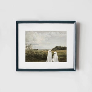 May include: A framed print of a painting depicting two white ghosts standing in a field with a cloudy sky in the background.