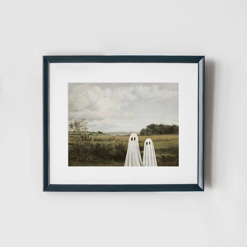 May include: A framed print of a painting depicting two white ghosts standing in a field with a cloudy sky in the background.