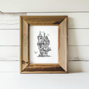 May include: A black and white line drawing of a whimsical house with a tower, a balcony, and birds flying around it. The house is framed in a rustic wooden frame.