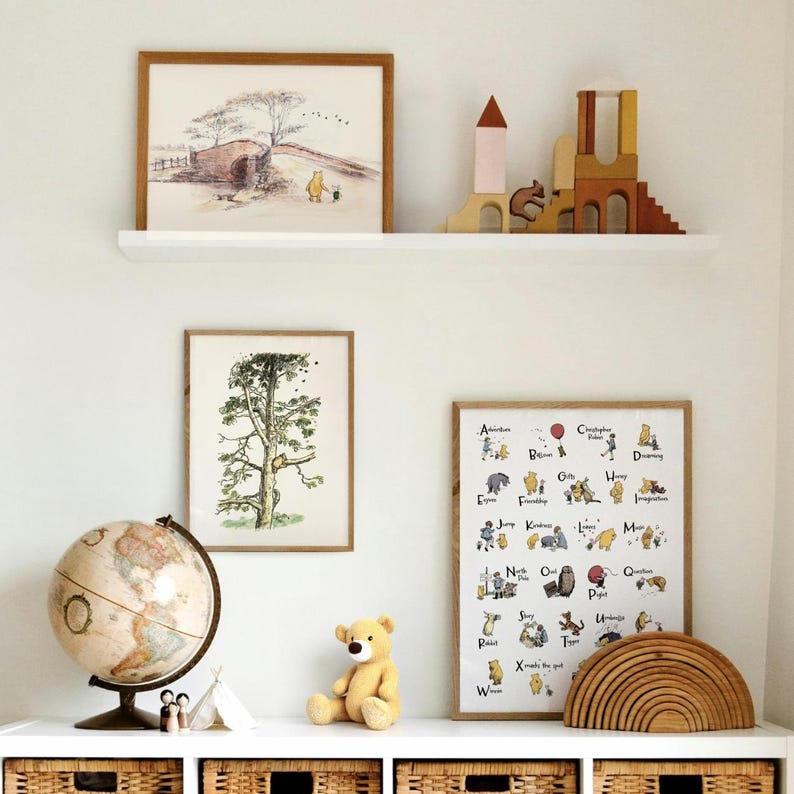 K&ouml;nnte beinhalten: Ein Kinderzimmer mit gerahmten Kunstwerken, Holzspielzeug und einem Globus. Die Kunstwerke umfassen einen Winnie-the-Pooh-Druck, eine Baumillustration und ein Alphabet-Poster. Ein gelber Teddyb&auml;r sitzt auf einem wei&szlig;en Regal.