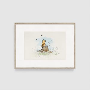 May include: Watercolor illustration of a yellow bear sitting on a tree stump, looking up at black dots. The artwork is framed in a light brown wooden frame.