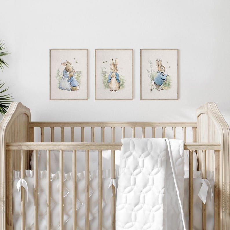 May include: Three framed prints of Peter Rabbit illustrations. The prints are in a nursery setting above a white crib with a white quilted blanket.