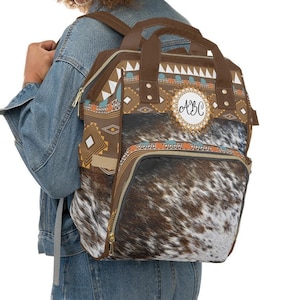 Personalized Distressed Brown and white tricolor faux cowhide tribal turquoise boho western style diaper bag backpack. Custom monogrammed with your name or initials.