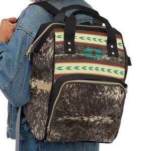 Personalized Brown and white tricolor faux cowhide tribal turquoise boho western style diaper bag backpack. Custom monogrammed with your name or initials. Faux animal print backpack.