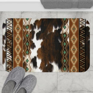 Puede incluir: Una alfombra de baño de piel de vaca marrón y blanca con un borde geométrico turquesa y marrón.