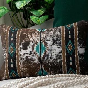 Peut inclure: Un coussin décoratif avec un motif de peau de vache marron, blanc et noir et des motifs géométriques turquoise et marron. Le coussin est rectangulaire et a une texture douce et moelleuse.