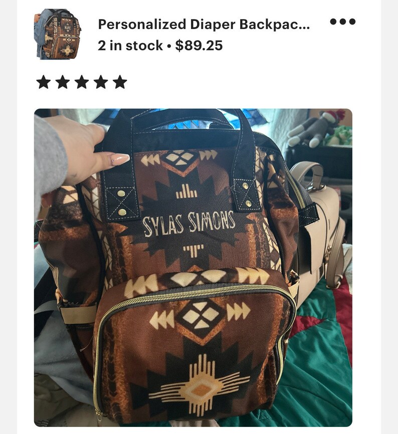 May include: A brown and black diaper backpack with a geometric pattern and the name "SYLAS SIMONS" embroidered on the front. The backpack has a large main compartment and several smaller pockets.
