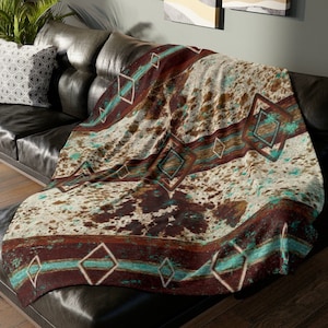 以下が含まれることがあります： 茶色、白、ターコイズの幾何学模様の入った毛布。この毛布は柔らかく、ふわふわした生地で作られており、どんな部屋にも暖かさとスタイルを加えるのに最適です。