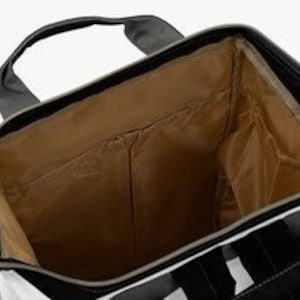 May include: The inside of a black and white striped diaper bag with a brown lining. The bag has a zipper closure and a large main compartment. There are several pockets on the inside of the bag, including a zippered pocket and a mesh pocket.