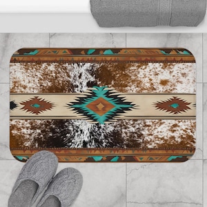 May include: A brown and white cowhide bath mat with a turquoise and brown geometric pattern. The mat has a fringed edge.