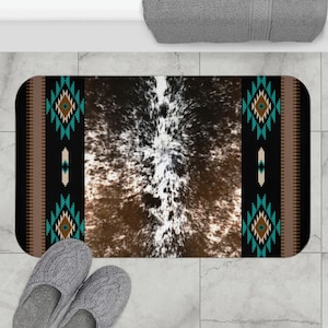 May include: A brown and white cowhide bath mat with a turquoise and brown geometric border. The mat is on a tiled floor.